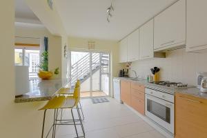 a kitchen with white cabinets and yellow bar stools at Penthouse Cassia in Cabanas de Tavira