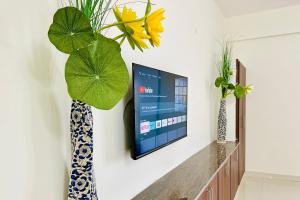 a tv on a wall in a living room with a plant at Tirupati Homestay - Ragunatha Resorts - 3BHK AC Apartments for large families - Best location - Flyover to Alipiri gate - Modular Kitchen - Super fast WiFi - Android TV - 250 Jio Channels - Easy access to visit all Temples in Tirupati