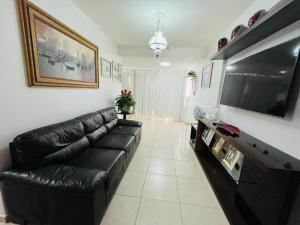 sala de estar con sofá de cuero negro y TV de pantalla plana en Cond. Beach Village Residence 1 en Fortaleza