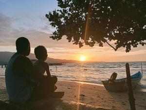 a man and a child sitting on the beach watching the sunset at Biryei Homestay in Pulau Birie