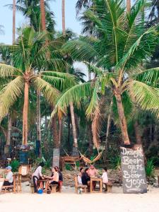 Leute sitzen an Tischen am Strand mit Palmen in der Unterkunft Oliver`s Laguna ECO Lodge Hotel in Ngapali