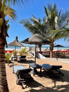 un grupo de mesas de picnic y sombrillas en una playa en Villa des Pêcheurs Beach Hôtel, en Cap Skirring