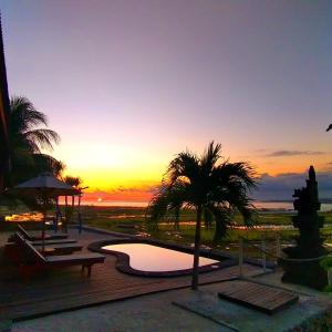 レンボンガン島にあるDouble'A beach houseのプールとヤシの木があるリゾートで、夕日を眺めることができます。