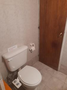 La salle de bains est pourvue de toilettes blanches et d'une porte en bois. dans l'établissement Aldos, à San Antonio Oeste