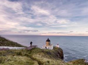 a man standing on a cliff next to a lighthouse at Romantic luxury Cottage right next to the ocean in Saint Abbs