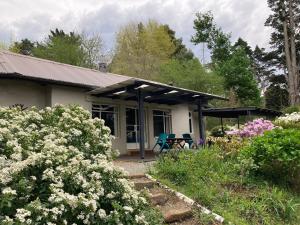 une petite maison blanche avec une véranda et quelques fleurs dans l'établissement Bramber Cottage Hogsback, Living With Joy!, à Hogsback