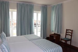 a bedroom with a bed and a chair and windows at Hotel Santo Antonio Da Baia in São Martinho do Porto