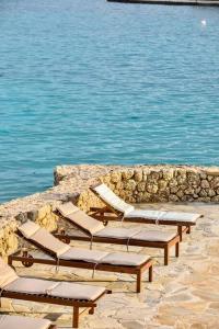 a row of chaise lounges and chairs next to the water at Vasiliki's Villa Beach Front and Pool in Porto Heli