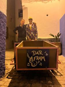 Due uomini in piedi accanto a una scatola con un cartello di Riad Dar Afram a Essaouira