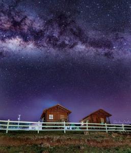 duas cabanas de madeira sob um céu noturno com a Via Láctea em Paraíso Dos Cânions em Bom Jardim da Serra