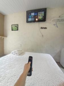 una persona con un mando a distancia frente a una cama en Suítes Caminho das Rosas Experiência na Montanha en Guapimirim
