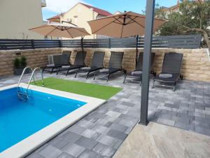 a pool with chairs and an umbrella on a patio at Apartmani Tropical in Vodice