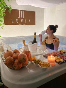 LUVIA ROOMS SPA في غونيسا: امرأة تجلس في حوض الاستحمام مع زجاجة من النبيذ