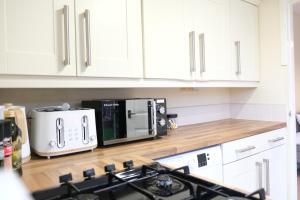 a kitchen with white cabinets and a stove and a microwave at Bee Stays - Maliston House in Great Sankey