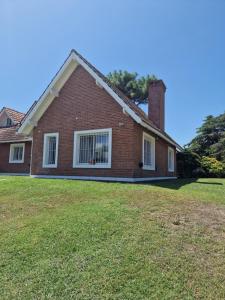 a red brick house with a grass yard at Dunas Chalet y Apartamento in Pinamar