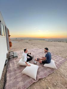zwei Männer sitzen auf einer Decke am Strand in der Unterkunft קסיופאה חוויה במדבר in Jerocham