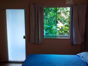a bedroom with a blue bed and a window at Suíte do Galo in Arraial do Cabo