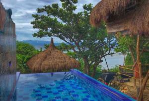 ein Pool mit einem Strohschirm und ein Resort in der Unterkunft Tree House by the Ocean ( for 2 guests) in Calatagan