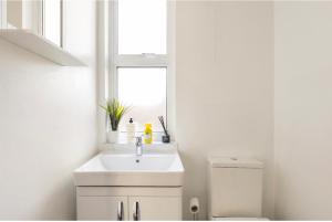 a white bathroom with a sink and a window at New renovated studio flat with separate kitchen and bathroom in Southall