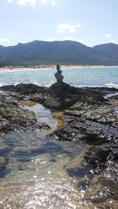 Buggerru Vacanze في بوجيرو: شخص يجلس على صخرة على الشاطئ