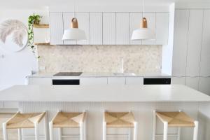 a white kitchen with a white counter and stools at Monterey Lodge - Unit 18, 27 Warne Terrace, Kings Beach Caloundra in Caloundra