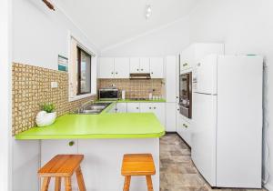 een witte keuken met een groene bar en 2 krukken bij Beachside Retreat in Gerringong
