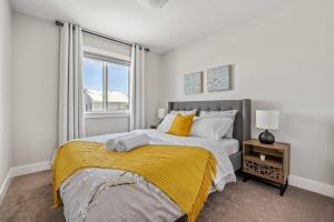 a bedroom with a bed with a yellow blanket and a window at Stylish 3BR Townhouse by Airport in Calgary