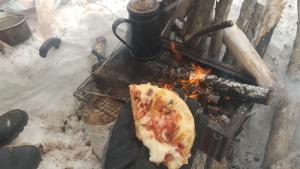 una persona sosteniendo una porción de pizza sobre un fuego en Ski base en Akaigawa