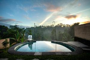 une piscine dans un jardin avec un coucher de soleil en arrière-plan dans l'établissement Campuhan Sebatu Resort, à Tegalalang