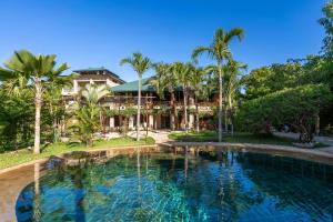 a swimming pool in front of a house with palm trees at Tombo House in Diani Beach