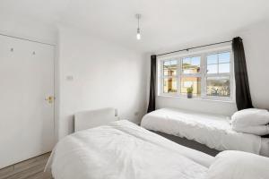 Cette chambre blanche dispose de 2 lits et d'une fenêtre. dans l'établissement Cozy Luton Town Centre Retreat, à Luton