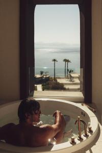 Ein Mann in einer Badewanne mit Meerblick in der Unterkunft Domes Miramare, a Luxury Collection Resort, Corfu - Adults Only in Moraḯtika