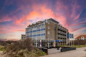 a building with a cloudy sky in front of it at Fletcher Hotel Restaurant Zeeduin in Wijk aan Zee