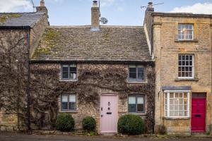 una vieja casa de ladrillo con una puerta rosa en Whitsun Cottage en Stow on the Wold