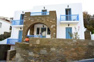 Biały dom z niebieskimi balkonami i kamienną ścianą w obiekcie Andros Guesthouses w mieście Andros