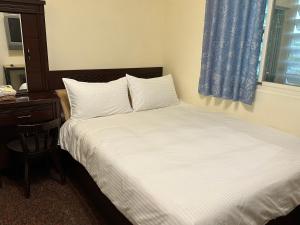 花蓮市にある偕安民宿のベッドルーム1室(白いベッド1台、デスク、窓付)