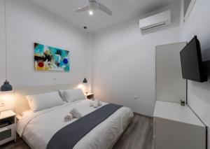 a white bedroom with a bed and a flat screen tv at Central Suites Aegina 2 in Egina