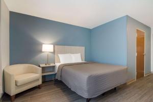 a blue bedroom with a bed and a chair at WoodSpring Suites Morrisville - Raleigh Durham Airport in Morrisville