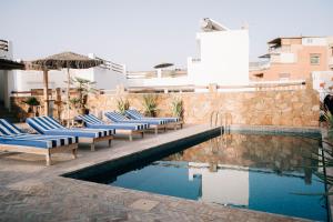 a pool with lounge chairs and an umbrella next to a building at Surf and Friends in Tamraght Ou Fella