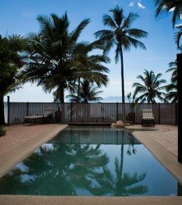 a swimming pool with palm trees and a fence at Rose Bay Resort in Bowen