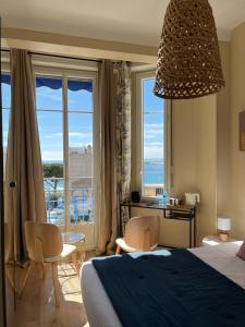 1 dormitorio con cama, sillas y ventana grande en Hôtel Eden - La Baigneuse, en Juan-les-Pins