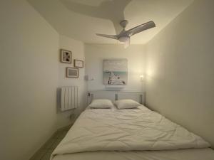 a white bedroom with a bed with a ceiling fan at Sol-y-Days Mayflower, Appartements bien équipés et climatisés, résidence avec piscine in Le Grau-du-Roi