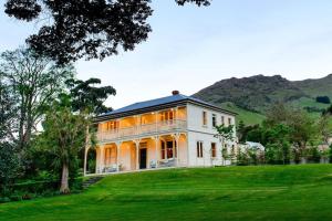 una gran casa blanca en una colina con césped verde en Annandale Coastal Farm Escape & Luxury Villa Collection, en Akaroa