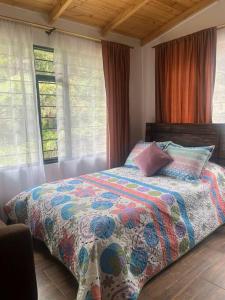 a bedroom with a bed with a colorful comforter and windows at Cabaña Campestre Montreal in Paipa