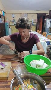 Une femme qui coupe de la nourriture dans un bol vert sur une table dans l'établissement Chacha Homestay & Dormitory, à Ruteng