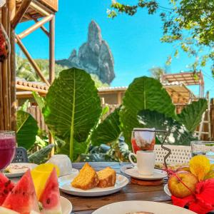 a table with plates of food and drinks and a mountain at Pousada Moana in Fernando de Noronha