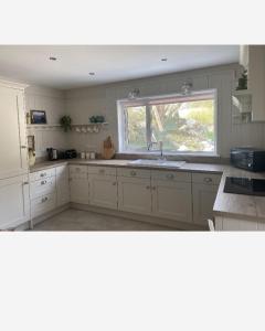 een witte keuken met een wastafel en een raam bij Stunning riverside cottage in central location in Donegal