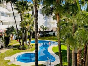 a pool with palm trees in front of a building at Apart Milla de Oro Marbella in Marbella