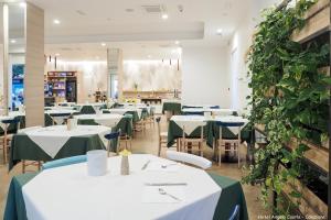 una sala da pranzo con tavoli bianchi e piante verdi di Hotel Angelo a Caorle