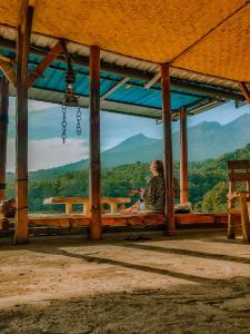 uma mulher sentada num banco a olhar para as montanhas em Rinjani Houseboon em Senaru